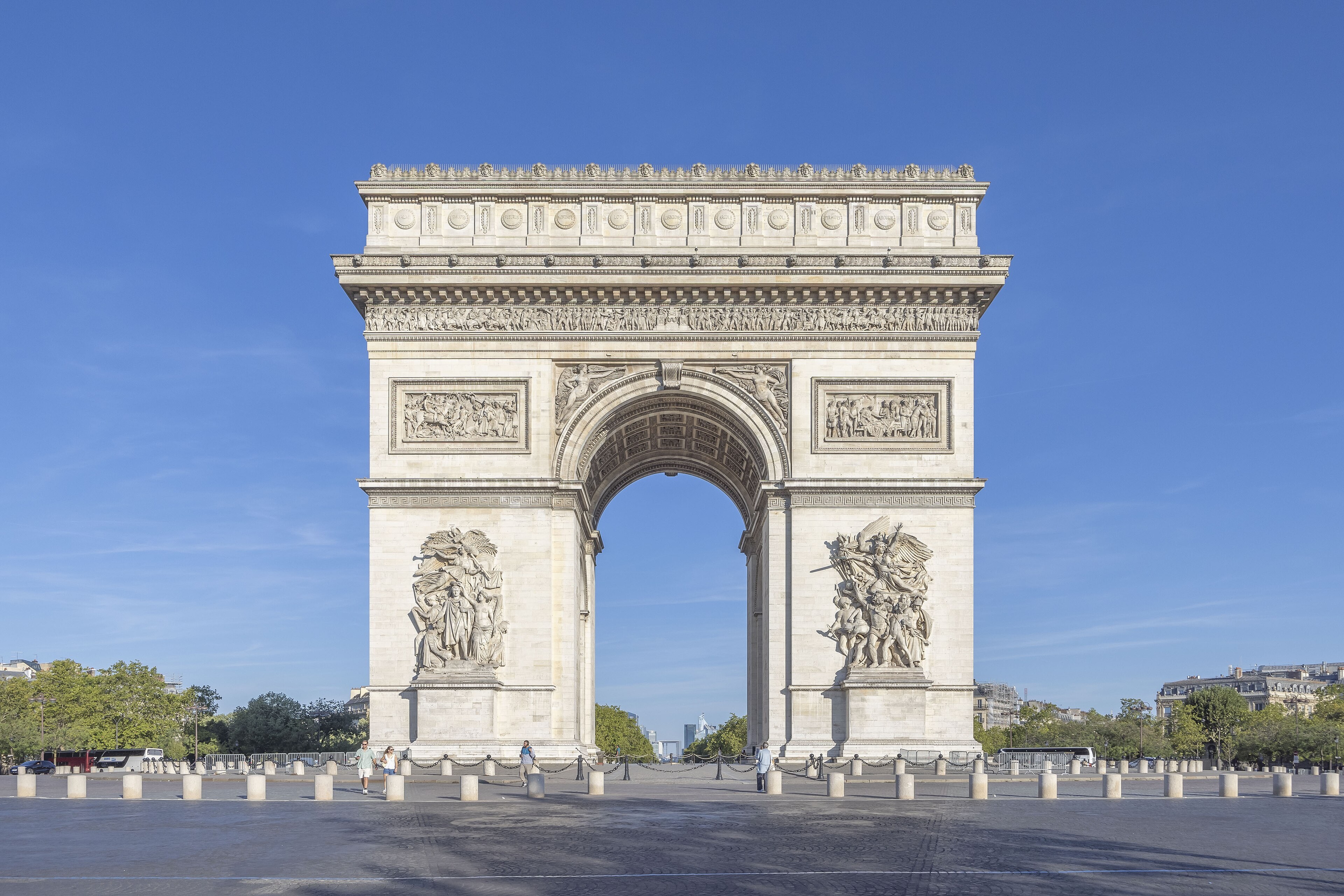 Arc de triomphe de l’Étoile de face, parvis piéton, plots, La Défense visible dans l’ouverture.